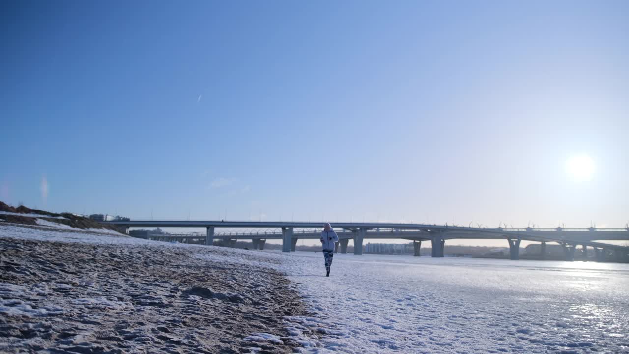 女孩在冬天沿着白雪覆盖的沙滩跑步视频素材