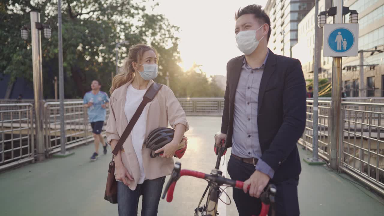 年轻的高中同学在城市立交桥上骑着自行车散步时偶然相遇，谈笑风生，两人都戴着防护口罩，健康生活在新常态下，生态节约视频素材