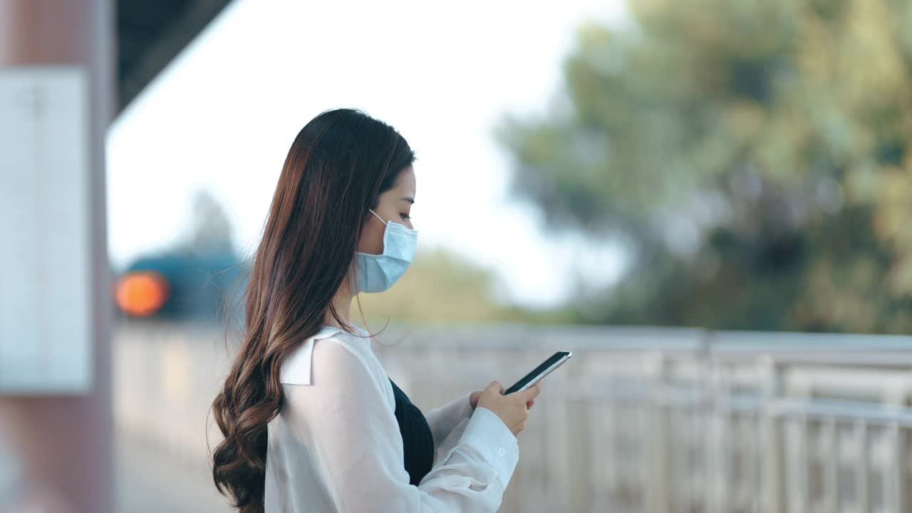 亚洲女性在地铁或火车通勤时，手持智能手机并佩戴外科口罩，保持社交距离视频素材