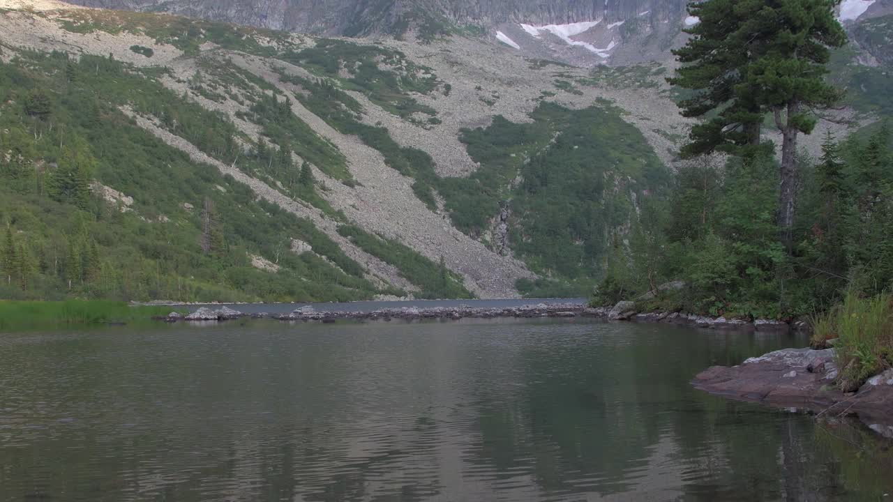 有森林山坡的山湖。雪松长在岸上，树叶随风飘动。表面布满了涟漪和波浪。透过清水可以看到花岗岩板视频素材