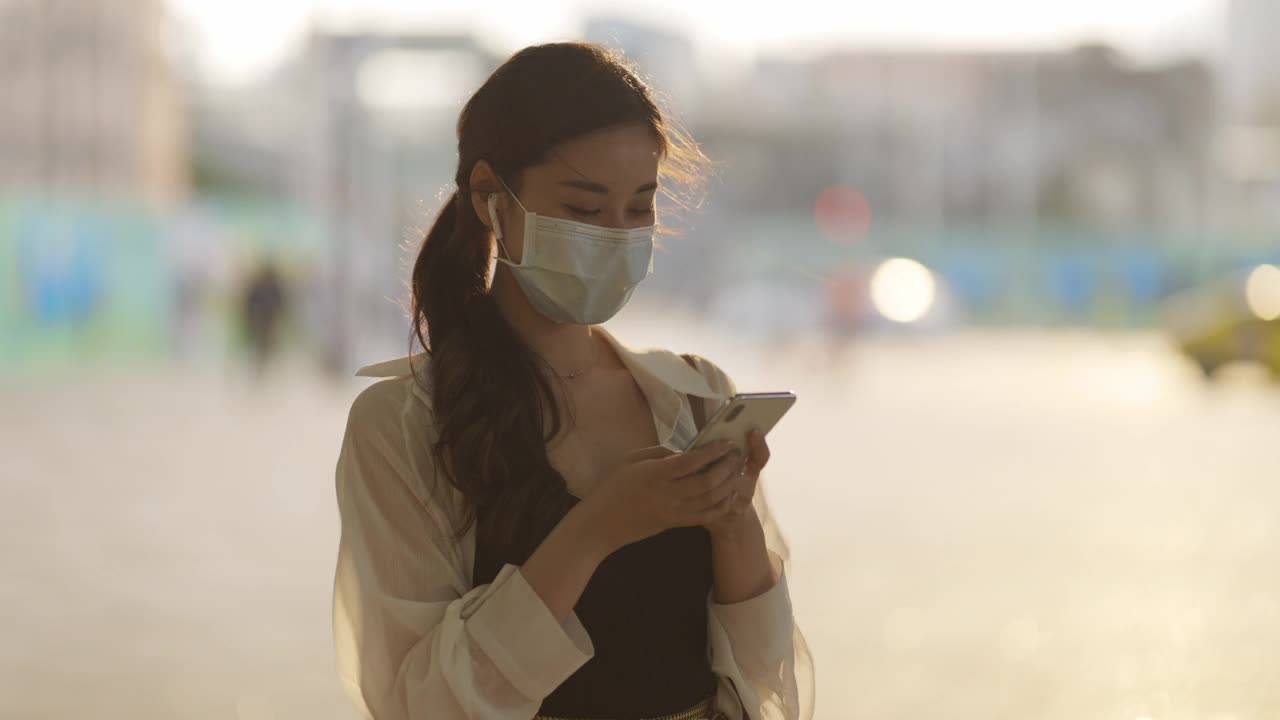 亚洲女性在地铁或火车通勤时，手持智能手机并佩戴外科口罩，保持社交距离视频素材