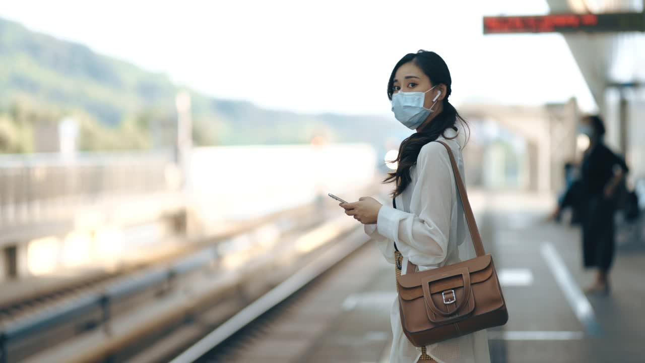 亚洲女性在地铁或火车通勤时，手持智能手机并佩戴外科口罩，保持社交距离视频素材