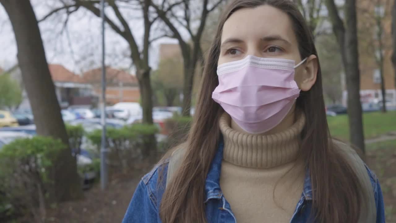 年轻女子戴着口罩走在街上看智能手机视频素材