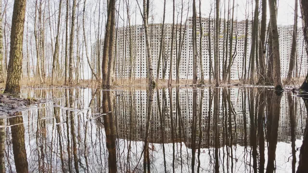 高楼层房屋的建设，从公园透过水中的树木，缓慢移动的摄像机，没有窗户和立面装饰的混凝土块，多云的天气视频素材