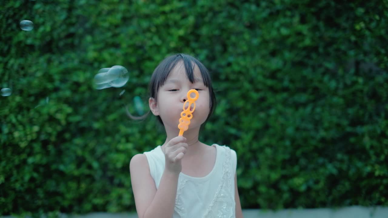 可爱的黑色长发亚洲女孩的肖像玩吹肥皂泡快乐的花园。视频素材