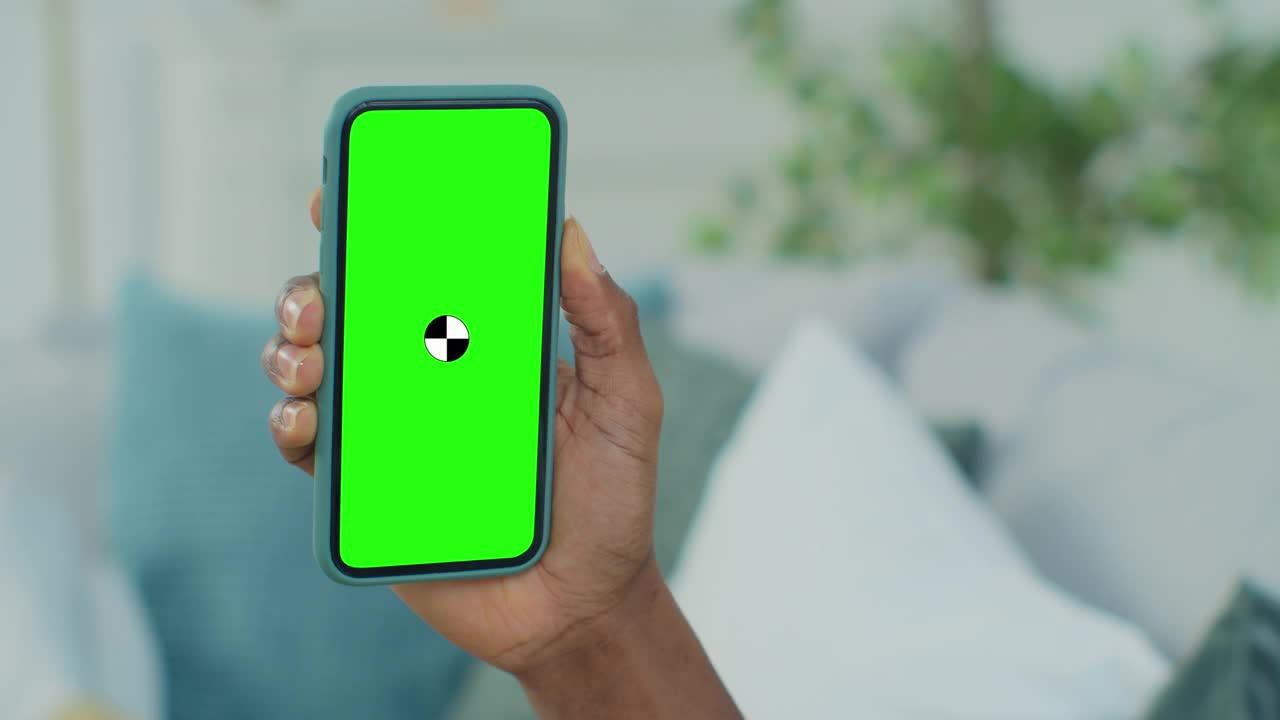 非洲裔美国人的观点，坐在沙发上使用智能手机与绿色模拟屏幕色度键上网观看内容视频。视频素材