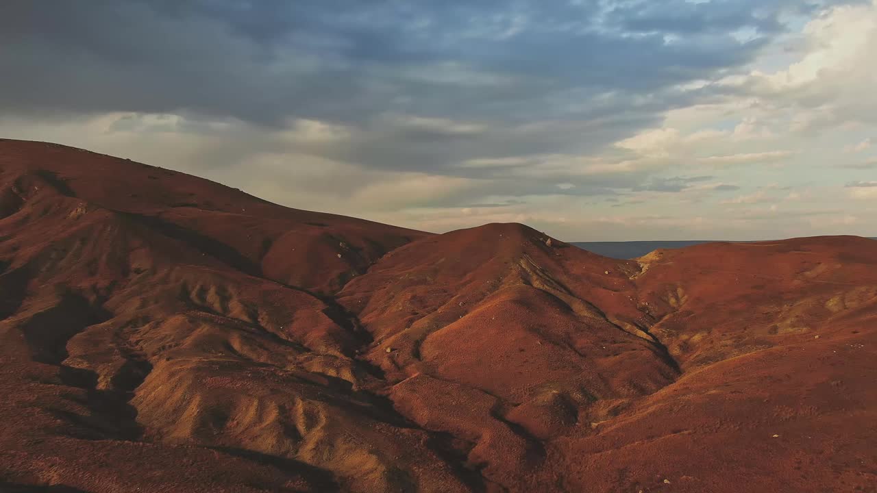 陌生的风景。鸟瞰图。在多云的天空下，在夕阳的光线下，飞过长满青草和石头的小山。视频下载