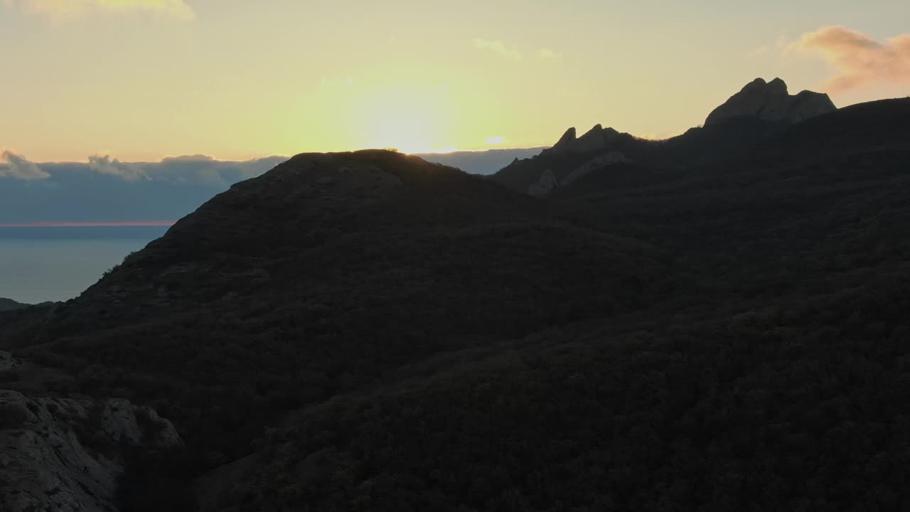 海上日出鸟瞰图，透过多云的海啸和山脉的海岸。一个令人愉快的景象。视频下载