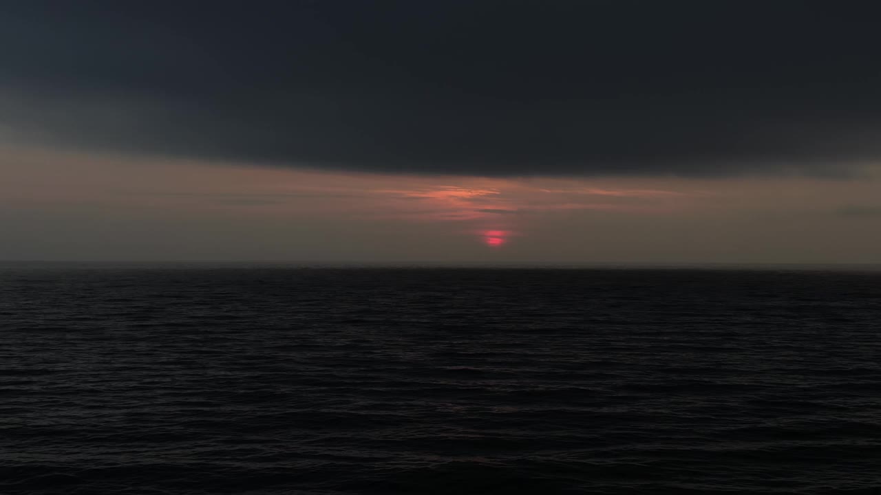 红色的太阳盘之间的波浪黑色的海和云的黑色天空在日出期间在海上地平线视频下载