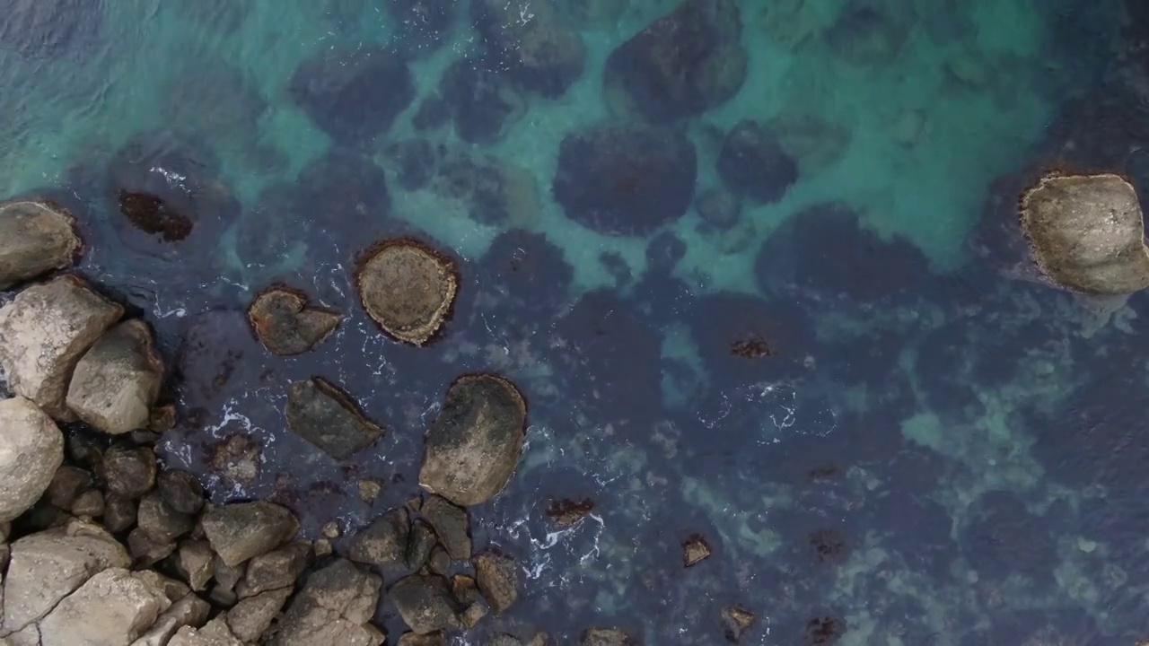 鸟瞰图的岩石海岸线，海浪溅在巨大的石头与藻类丛生视频下载