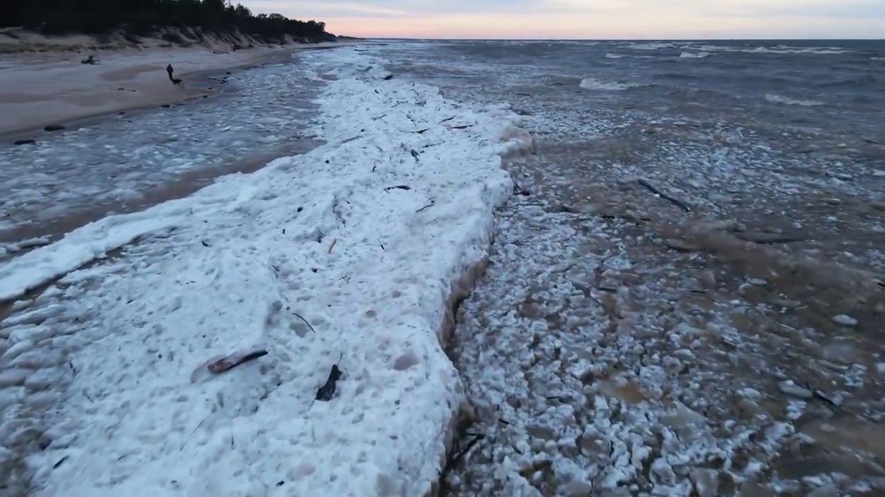 一名男子遛着他的狗沿着冰漂流在有风的天气和海浪在海上视频素材