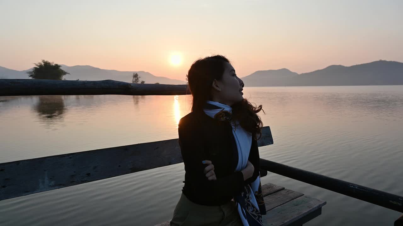 年轻的亚洲女人放松和呼吸在木码头，日出在山区湖泊在农村视频素材