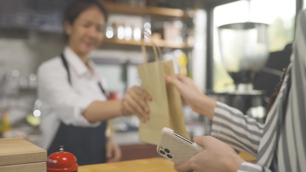 在咖啡馆美丽的亚洲女人使外卖咖啡的客户谁支付手机系统视频下载