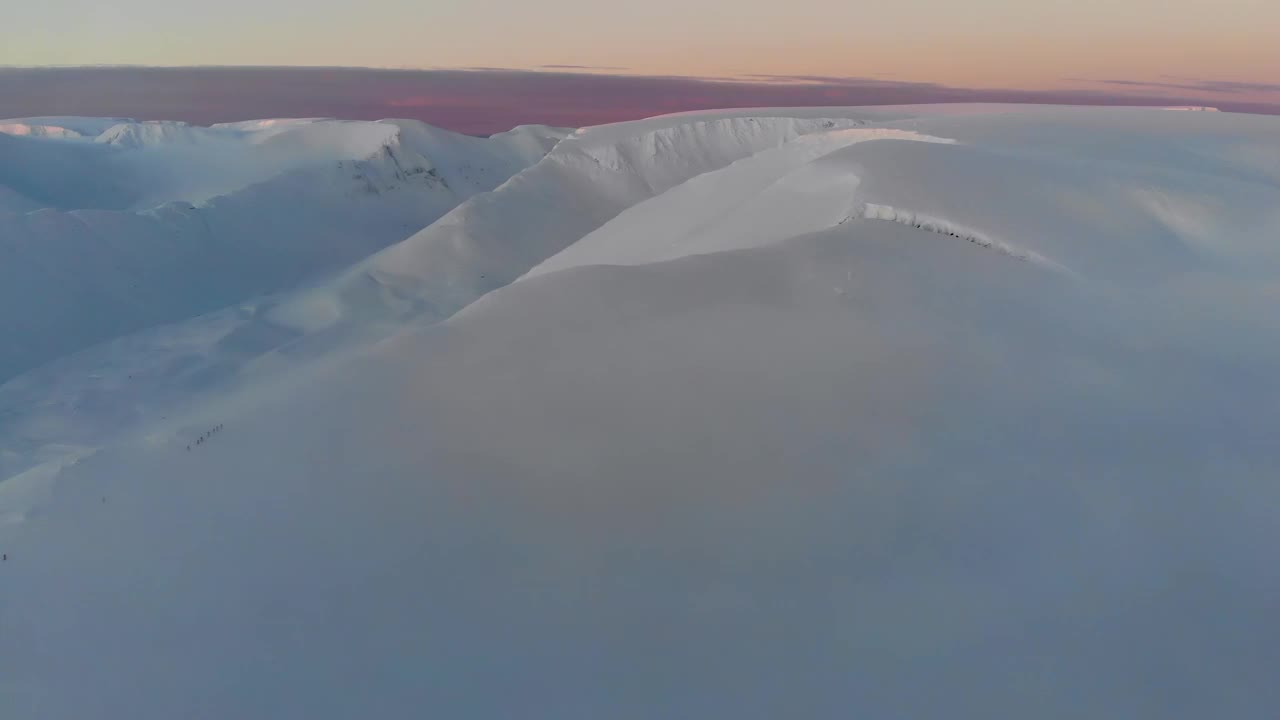 在日落时飞过白雪皑皑的山脉。鸟瞰图。山上五颜六色的冬季日落。视频下载