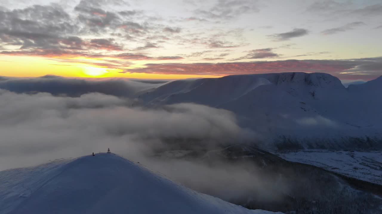 在夕阳中飞过白雪皑皑的山峰。鸟瞰图。山上五颜六色的冬季日落。视频下载