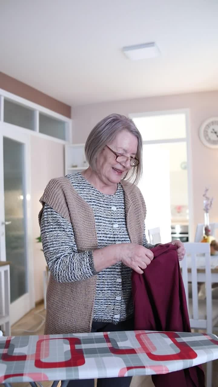 熨烫衣服的老女人。家里家务。一个年老的成熟妇女的肖像，她熨衣服和做日常家务-真正的普通人视频素材