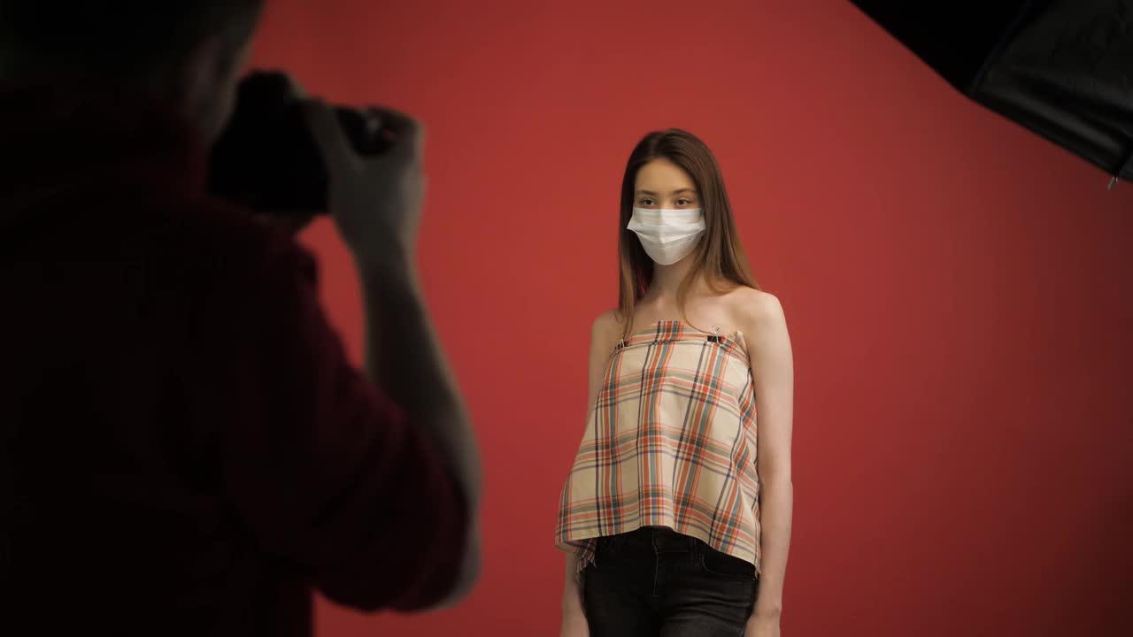 新冠肺炎疫情口罩妇女隔离自动隔离病毒，在工作室工作的年轻学生模特，摄影师正在拍摄戴口罩的学生女孩视频购买
