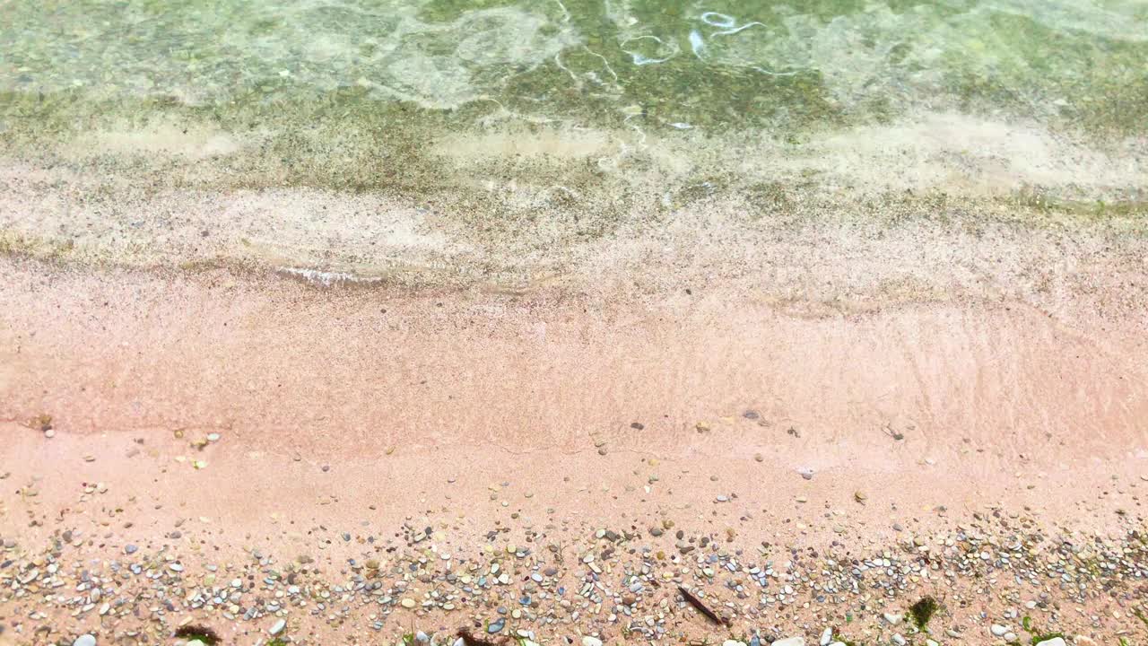 海岸附近缓慢的海浪和粉红色和绿色的沙子视频下载