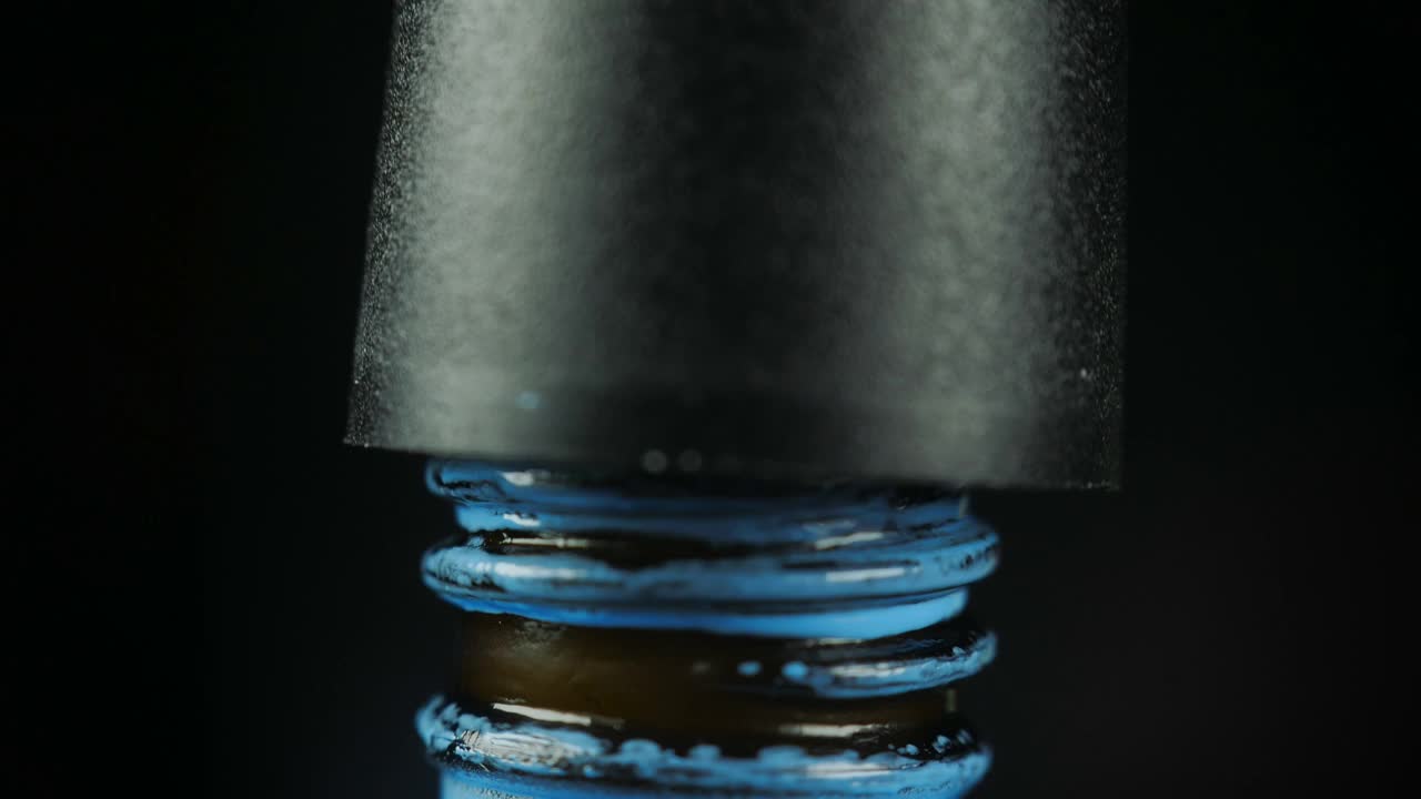 在美容院用开瓶的蓝色凝胶指甲油，用刷子滴一滴到罐子里。黑色背景。特写镜头。视频下载
