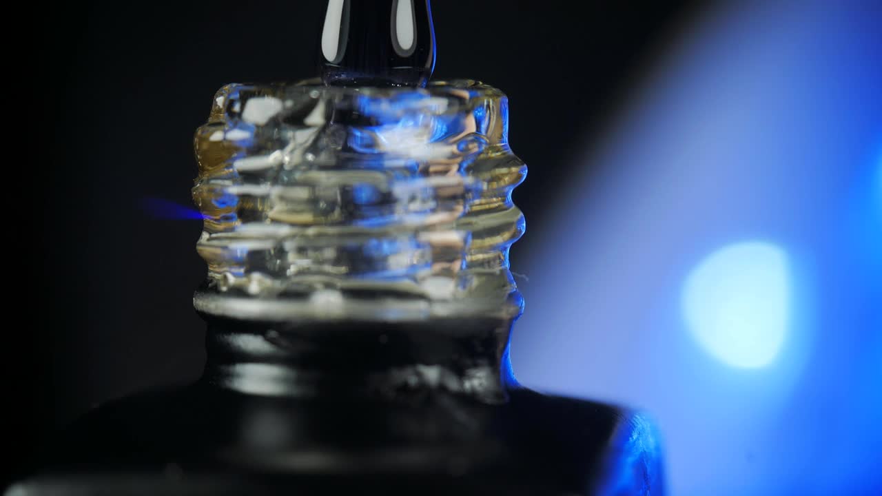 透明凝胶指甲油与一个打开的瓶子和一滴滴到一个罐子与刷子在美容院。背景蓝色LED灯。特写镜头。视频下载