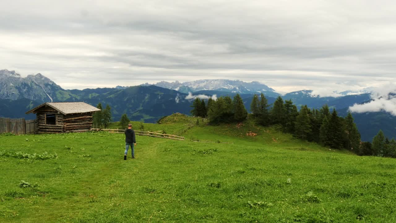 在奥地利阿尔卑斯山美丽的山景中，一个人带着小屋走过草地视频下载