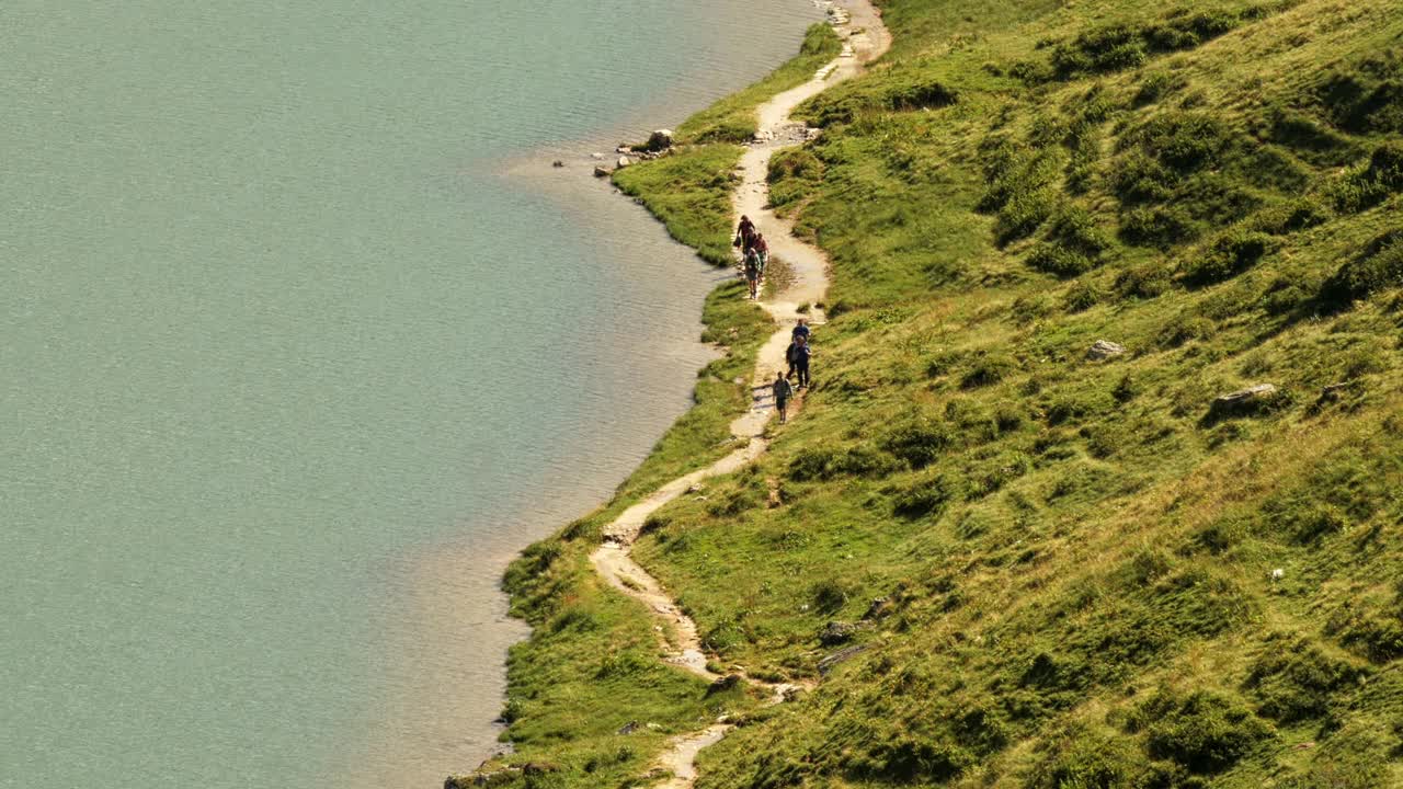 一群徒步旅行者在奥地利阿尔卑斯山的塔彭卡湖岸边的一条小路上——从上面拍摄的宽度视频下载