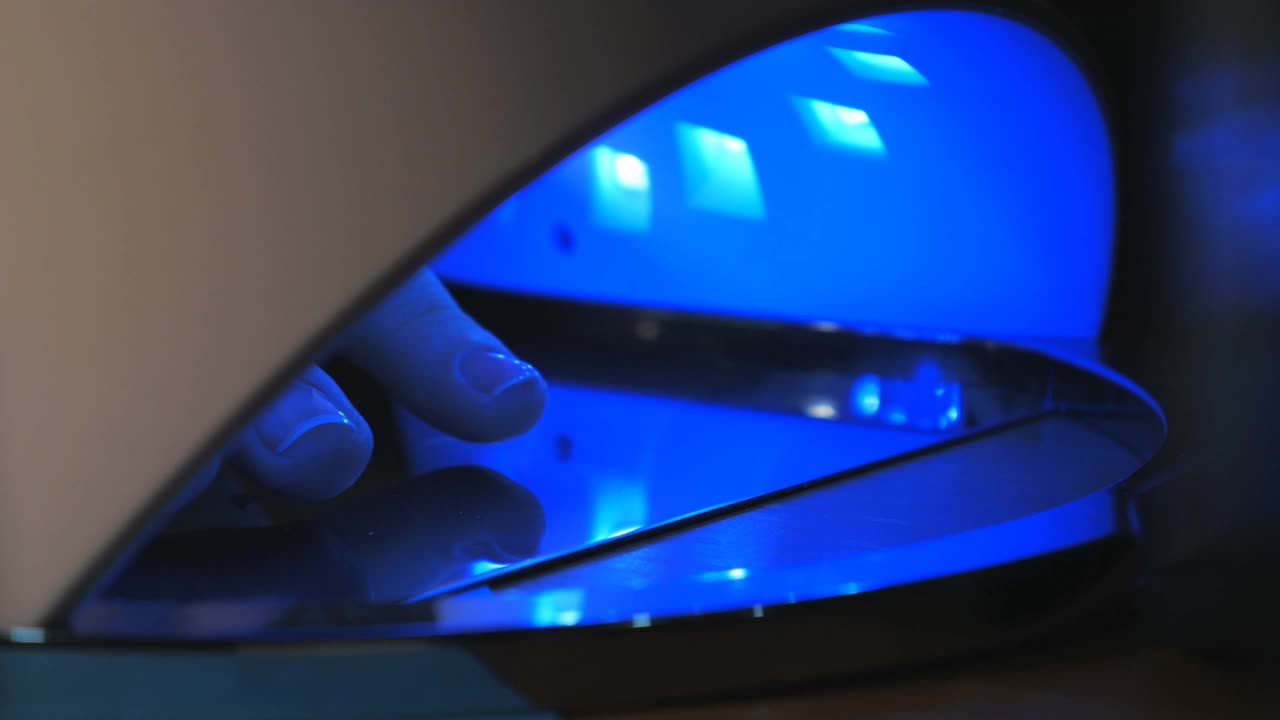 由于led灯的蓝光，女性的蓝色指甲和皮肤特写。技术固化和干燥美甲UV灯覆盖现代时尚的指甲油凝胶。视频下载