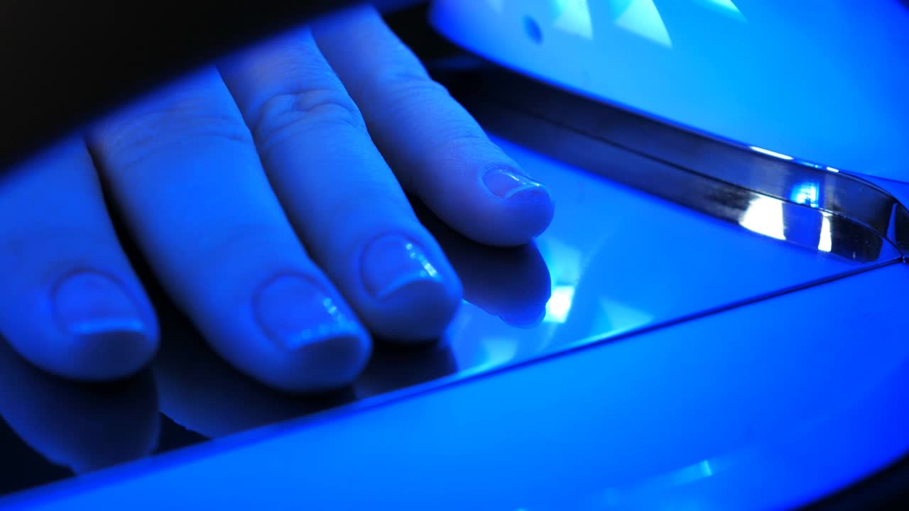 由于led灯的蓝光，女性的蓝色指甲和皮肤特写。技术固化和干燥美甲UV灯覆盖现代时尚的指甲油凝胶。视频下载