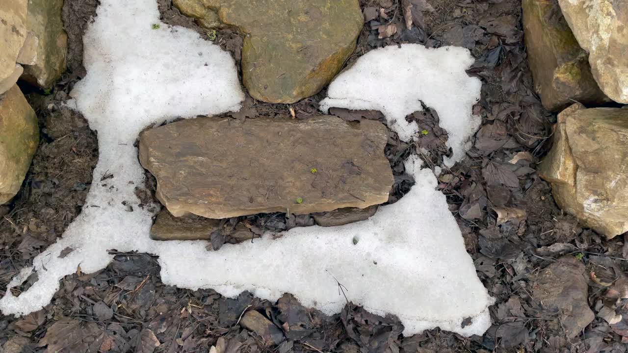 乡间通往一座缓坡的路上，有部分积雪覆盖着平坦的大石头视频下载