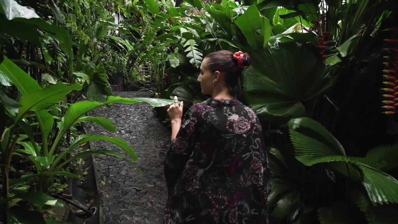 美丽的女孩在丛林里穿过热带植物。女人在生态度假村发现雨林花园。慢镜头丛林徒步旅行视频下载