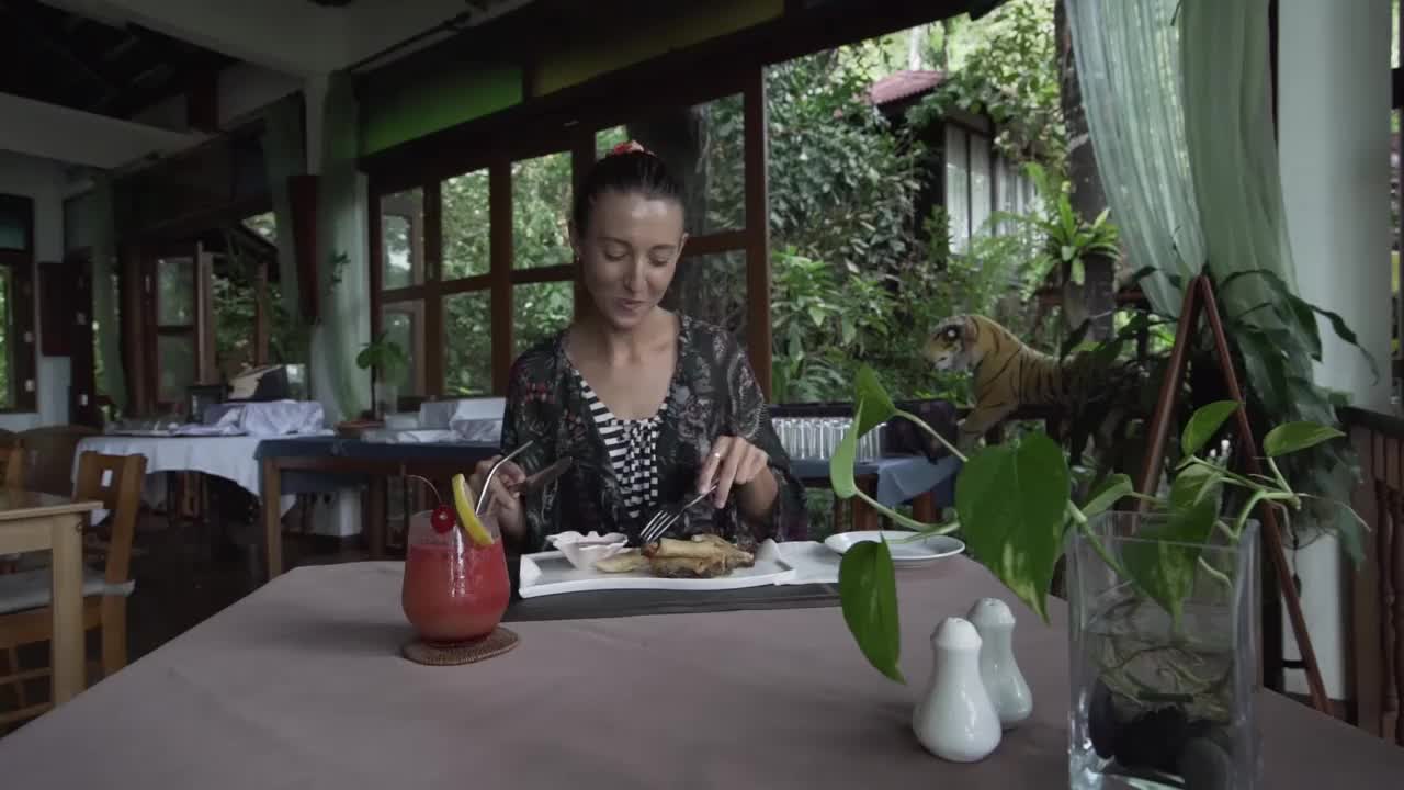 美丽的女人在豪华酒店餐厅吃早餐，外面有令人惊叹的热带雨林景色。视频下载