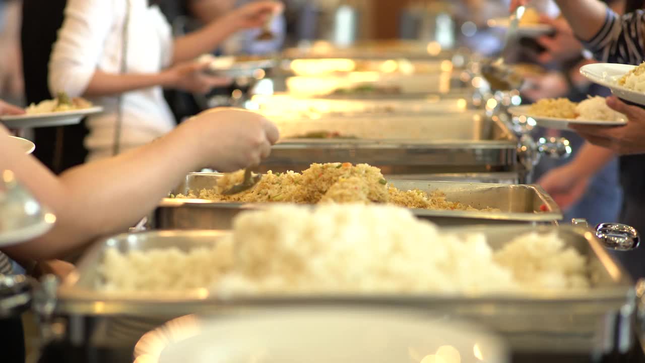 一群人在自助餐队伍中排队舀食物。专注于每个舀食物的人的手。视频下载