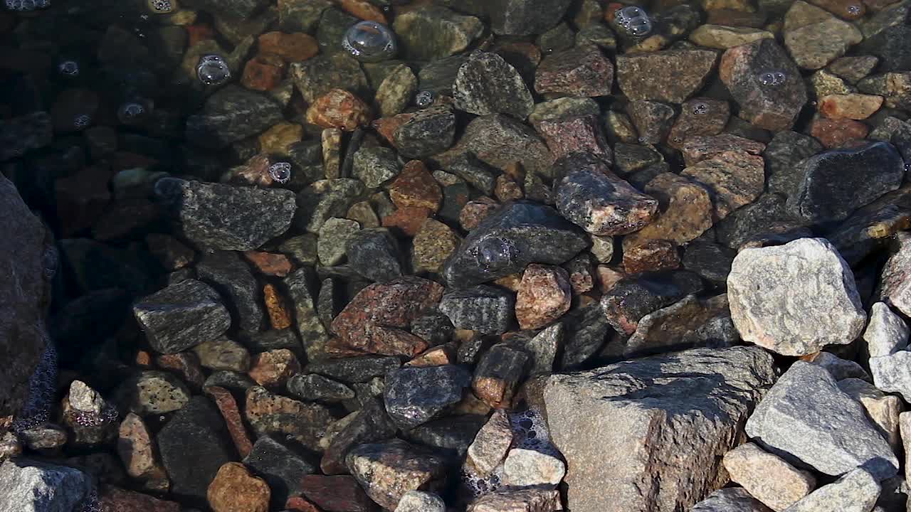 平静的海浪之间的石头在白天，冲洗海岸，苔藓和藻类的自然背景视频下载