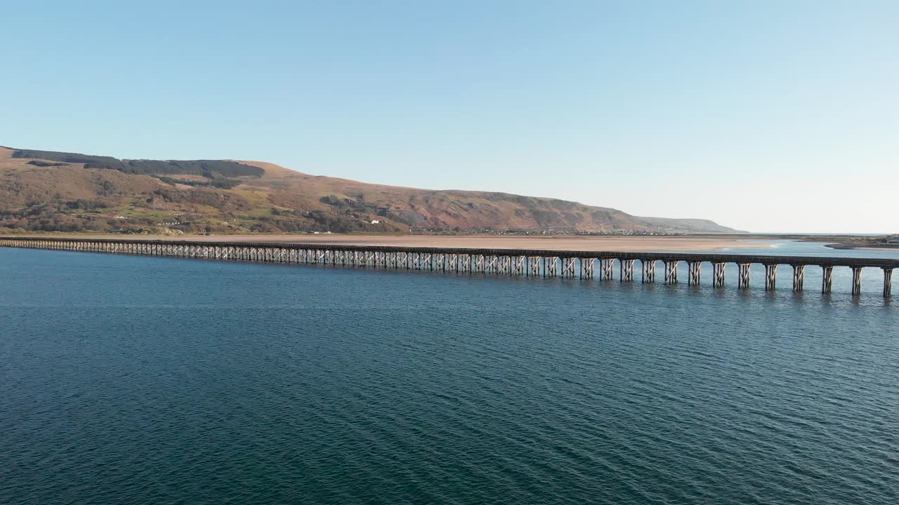 Barmouth bridge (viaduc)威尔士和壮丽的山脉和蓝色的水在美丽的蓝天下的风景向后镜头视频下载