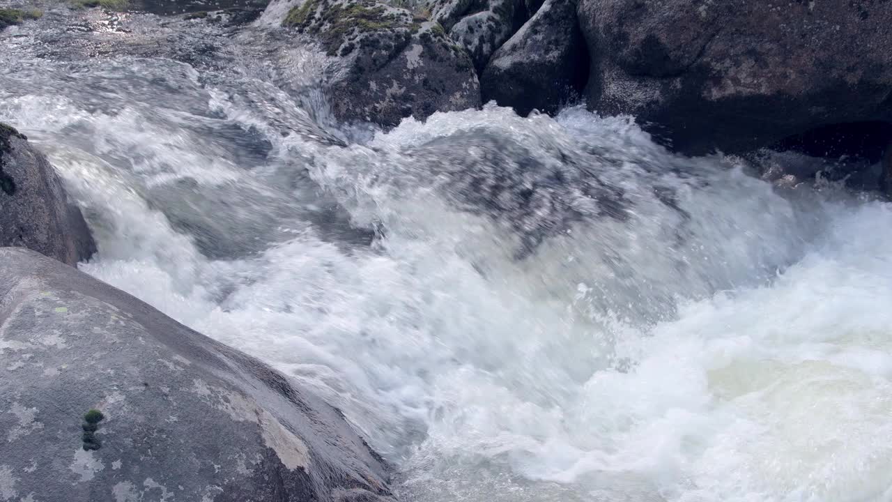 灰色岩石间湍急的水流。悬崖上长满了苔藓。山河撞击岩石，形成水花和泡沫。水元素的自然力和能量视频下载