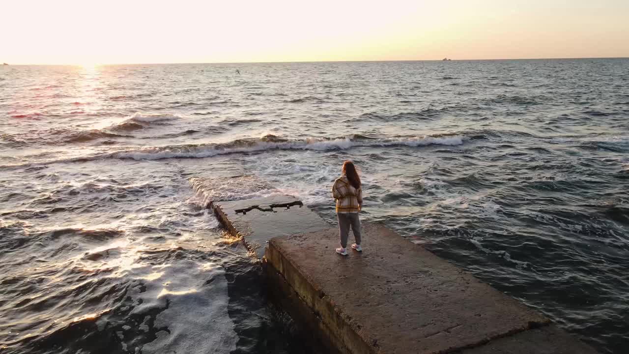 年轻女子在美丽的日出在海上的石头码头视频下载