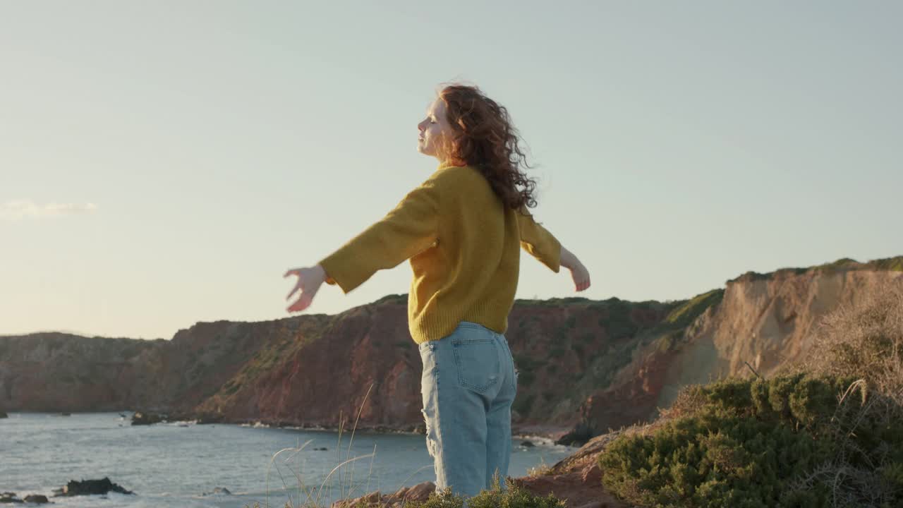 年轻女子在海边悬崖上享受海风视频素材