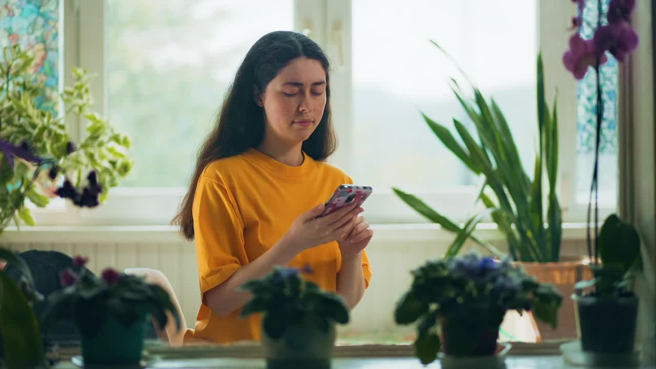 微笑的年轻白人妇女在家里用手机交流。室内有天然植物。背景中的一个窗口。真正的时间。沟通的概念视频素材