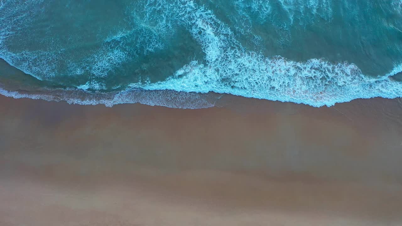 鸟瞰蓝色的大海，海浪拍打着海滩。视频素材