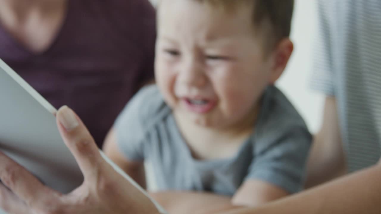 哭闹的小孩和父母一起坐在床上看平板电脑视频素材