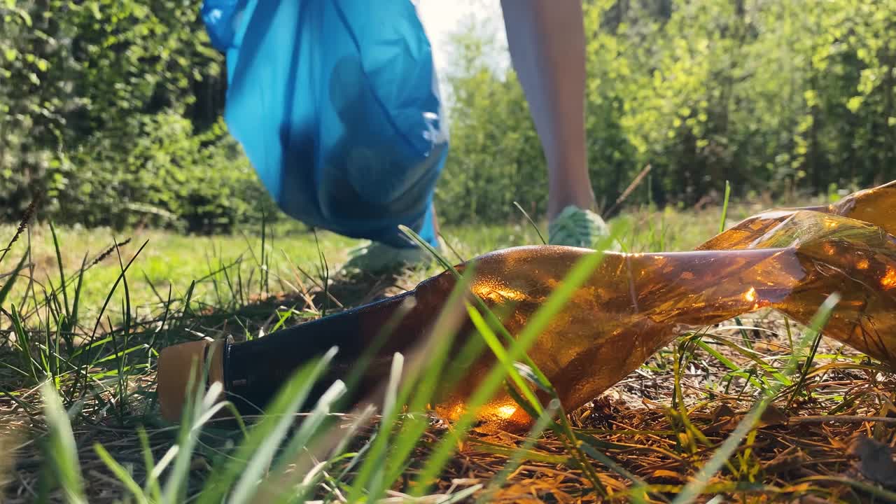 一个女孩在森林里捡垃圾，在夏天，慢镜头。一名志愿者在大自然中收集塑料瓶。从垃圾中拯救地球。环境问题的概念视频下载