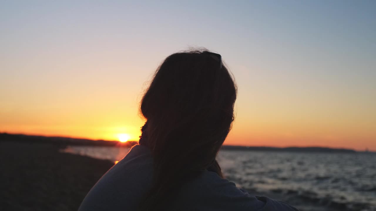 年轻女子独自坐在海边沙滩上看地平线在金色的日落视频素材