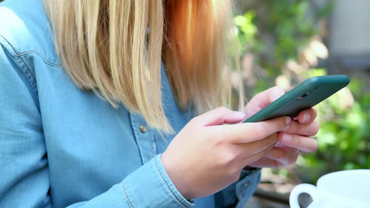 一位年轻女子的手触碰着智能手机的屏幕。年轻的金发女人在她的智能手机上写信息或网上购物视频下载