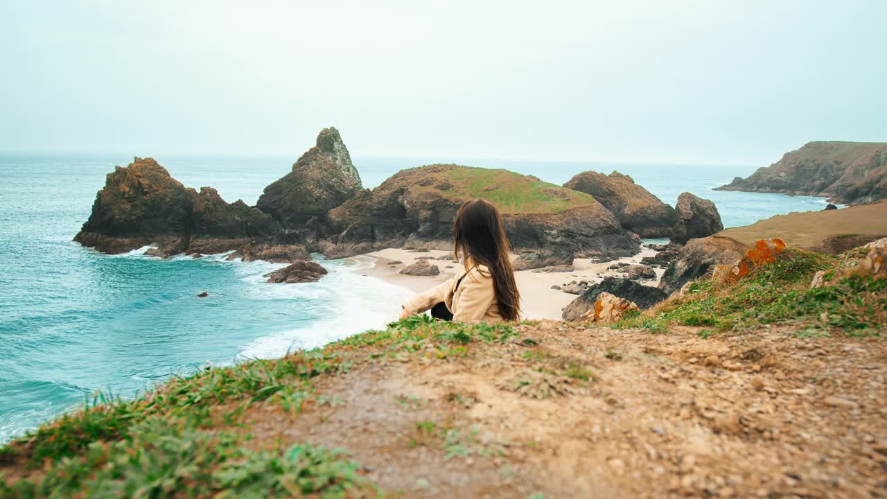 一位年轻女子坐在金尼斯湾边欣赏风景。视频素材