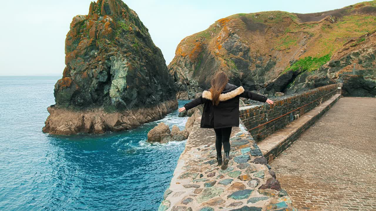 一个美丽的女孩走在风景优美的海港边上。视频素材