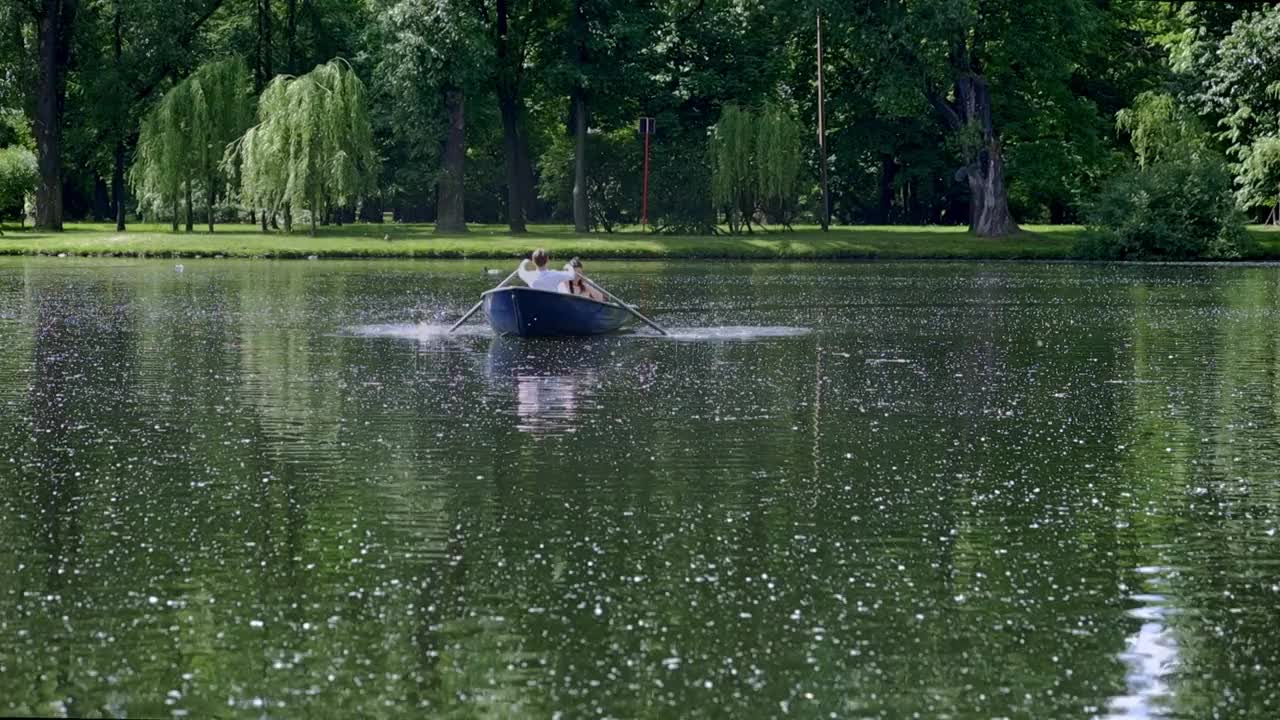 乘坐一艘船在夏天在一个池塘在公园，一个年轻人划船在桨高质量的全高清镜头视频下载