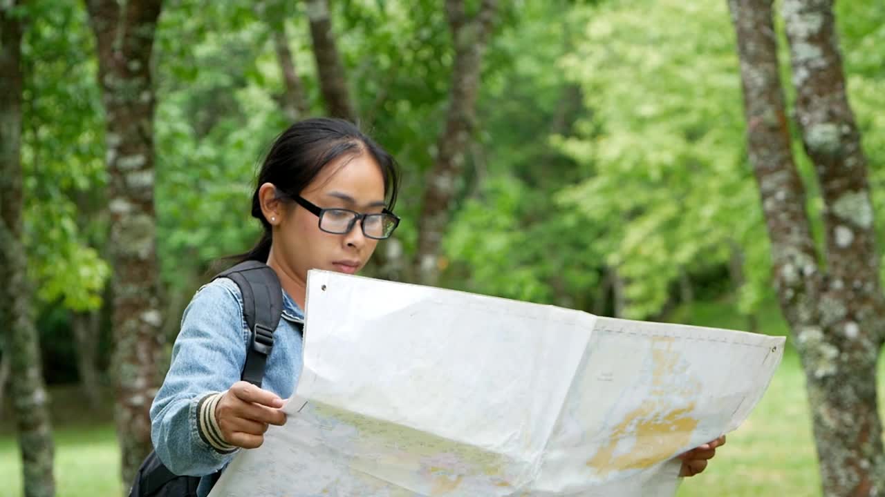 一名背着背包的女游客在森林里放松，在地图上寻找正确的方向。旅游和度假的生活方式的概念。视频素材