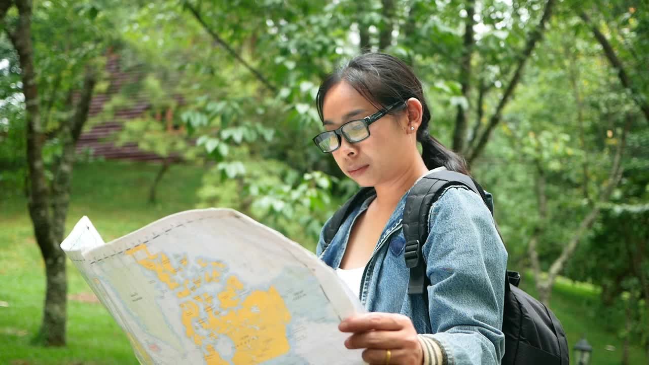 一名背着背包的女游客在森林里放松，在地图上寻找正确的方向。旅游和度假的生活方式的概念。视频素材