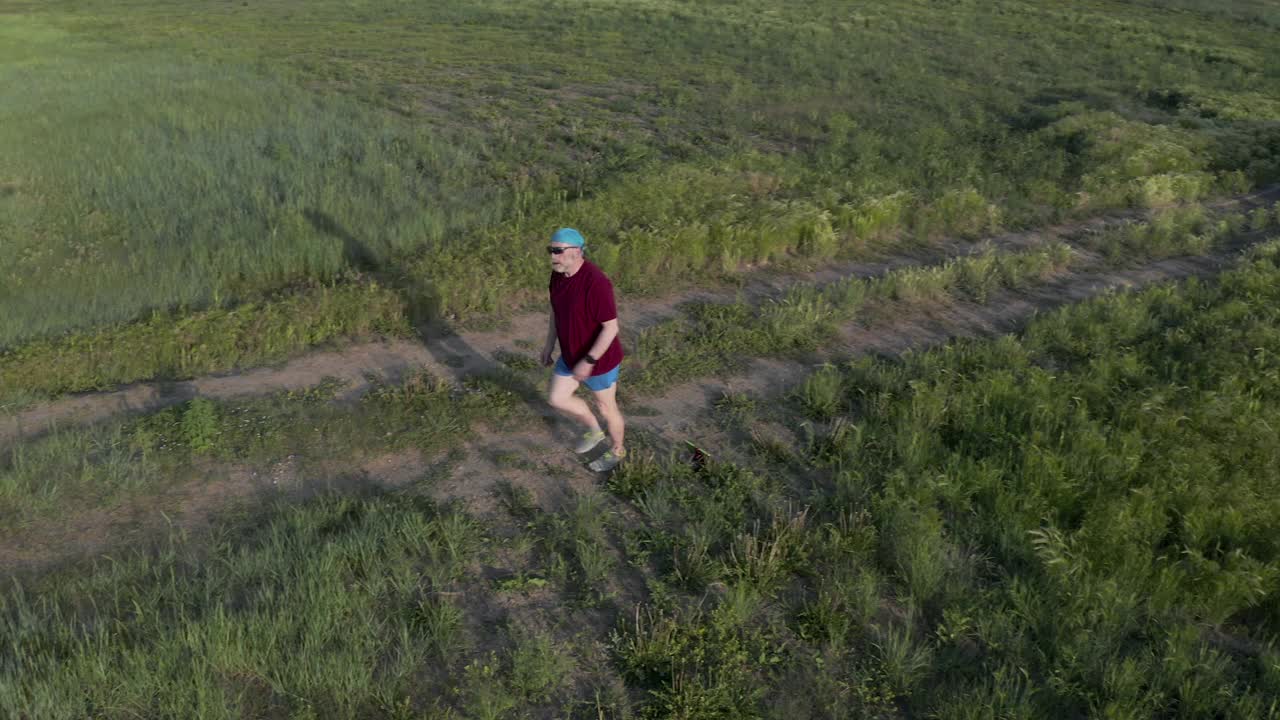 年长的，运动的，超重的男性正在穿越绿色草原的小路上跑步视频素材