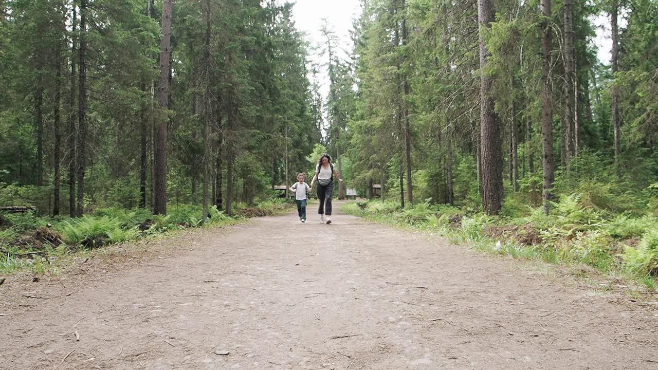 幸福的家庭年轻友好的母亲和女儿跑到户外的相机通过森林公园手牵手在森林公园。孩子梦想，自由或家庭幸福一起的理念。慢动作视频下载